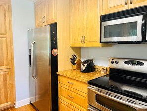 A kitchen with wooden cabinets, a stainless steel refrigerator, a microwave, a toaster, and an oven. - Fairway To Heaven 3 Bedroom Home by RedAwning (Supply)