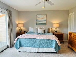 A bedroom with a bed, two bedside tables, a ceiling fan, a painting, and a window with curtains.