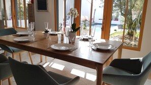 A dining table set with plates, cutlery, and glassware, surrounded by chairs, with a view of a pool and greenery through large windows. - Villa with a pool, 7 km from La Rochelle and 15 km from Île de Ré (Dompierre-sur-Mer)
