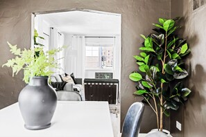 Un coin repas avec une table blanche, un vase gris contenant des plantes vertes et un radiateur noir.