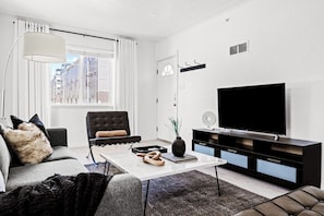 A modern living room with a sofa, armchair, coffee table, and a flat-screen TV.