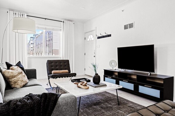 Una sala de estar moderna con un sofá, un sillón, una mesa de centro y un televisor de pantalla plana.