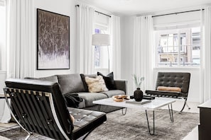A modern living room with a grey sofa, black armchair, and a white coffee table.