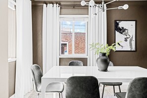 Ein Essbereich mit einem weißen Tisch, grauen Stühlen, einer Pflanzvase und einem gerahmten Bild an der Wand.