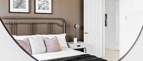 A bedroom with a bed, a bedside table, a nightstand, and a door leading to another room.