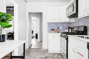 Una cocina moderna con armarios blancos, piso con diseño de espiga y salpicadero azulejado.