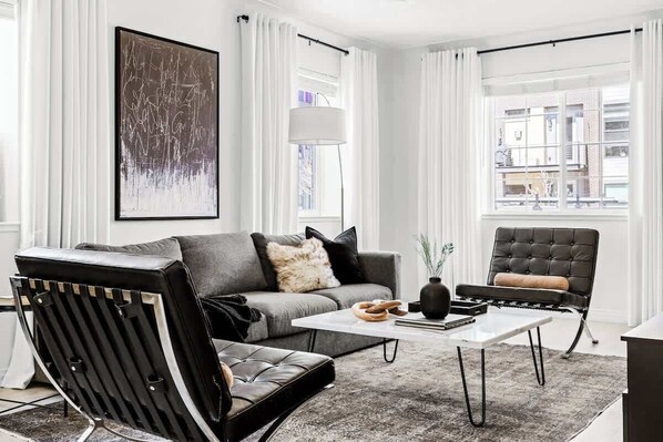 Un salon moderne avec un canapé gris, un fauteuil en cuir noir et une table basse blanche.
