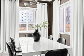 Un espace repas moderne avec une table blanche, des chaises noires et un vase noir orné de plantes vertes.