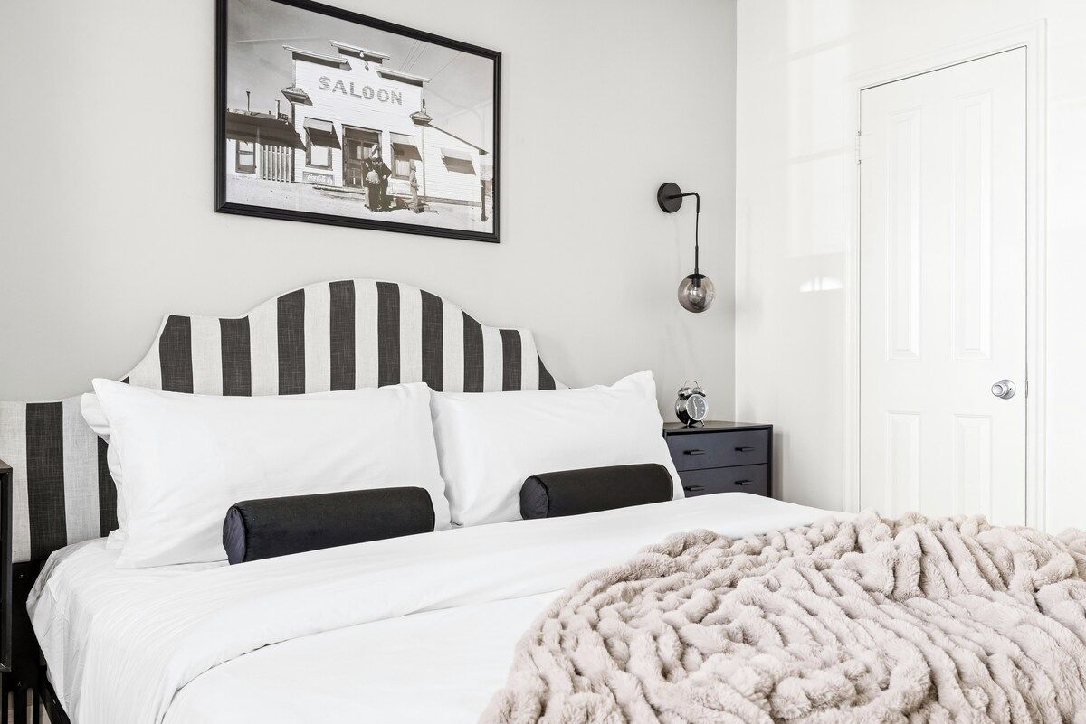 A bedroom with a bed, a nightstand, a wall-mounted lamp, and a framed picture.