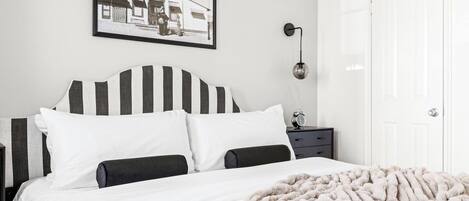 A bedroom with a bed, a nightstand, a wall-mounted lamp, and a framed picture.
