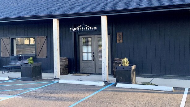 A building with a dark exterior, a front door, and two planters with small plants. - Sidelines @ Grand Park Game Room, Outdoor Basketball Court Sleeps 13+ (Sheridan)