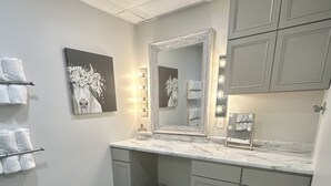 A bathroom with a vanity, mirror, and lighting. There are towels on the wall and a trash can. - Sidelines @ Grand Park Game Room, Outdoor Basketball Court Sleeps 13+ (Sheridan)
