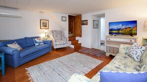 Ein Wohnzimmer mit einem blauen Sofa, einem blumigen Sofa, einer Holztreppe und einem Fernseher auf einem Tisch.