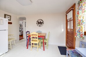 Uma sala de jantar com mesa e cadeiras de madeira, um relógio de parede e uma porta com cortina florida.