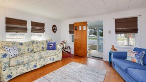 Ein Wohnzimmer mit einem blumengemusterten Sofa, einem blauen Sofa und einer Holztür, die nach draußen führt.