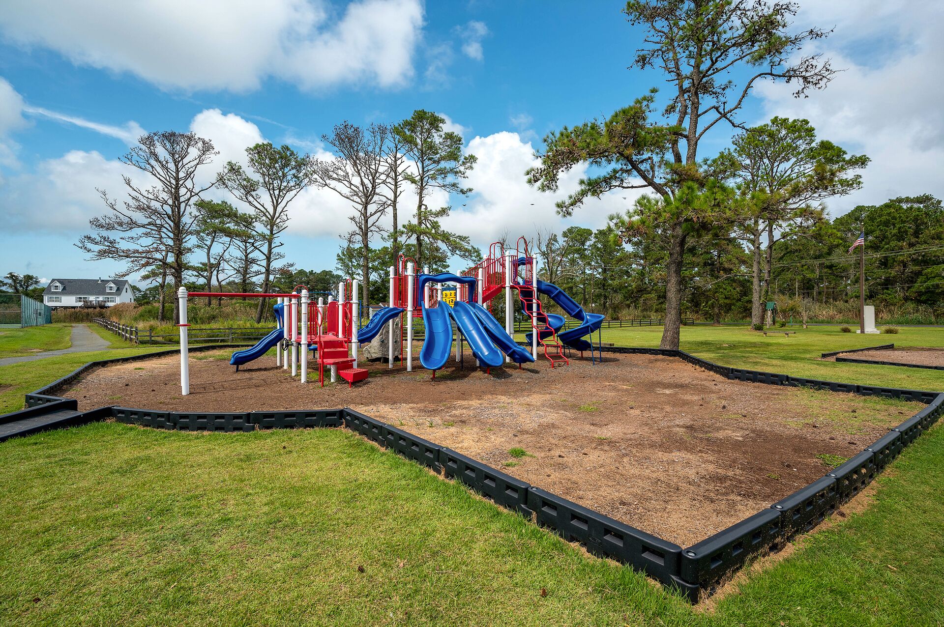 Un parque infantil con toboganes y estructuras para escalar, rodeado de césped y árboles.