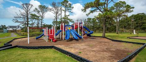 Un parque infantil con toboganes y estructuras para escalar, rodeado de césped y árboles.