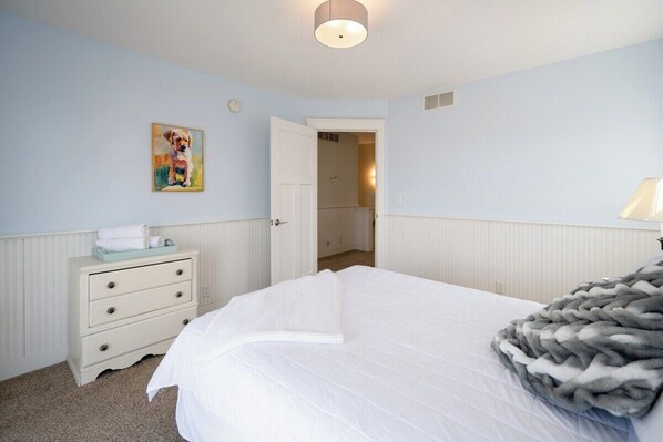Un dormitorio con cama, cómoda, un cuadro y una puerta que da a otra habitación.