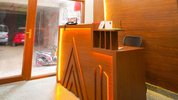 A reception desk with a wooden finish and a modern light fixture above it. - Roomshala 045 Galaxy Noida 35 (Noida)