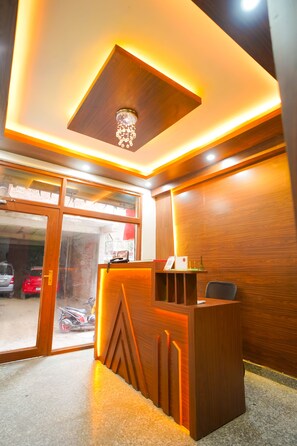 A reception desk with a wooden finish and a modern light fixture above it. - Roomshala 045 Galaxy Noida 35 (Noida)