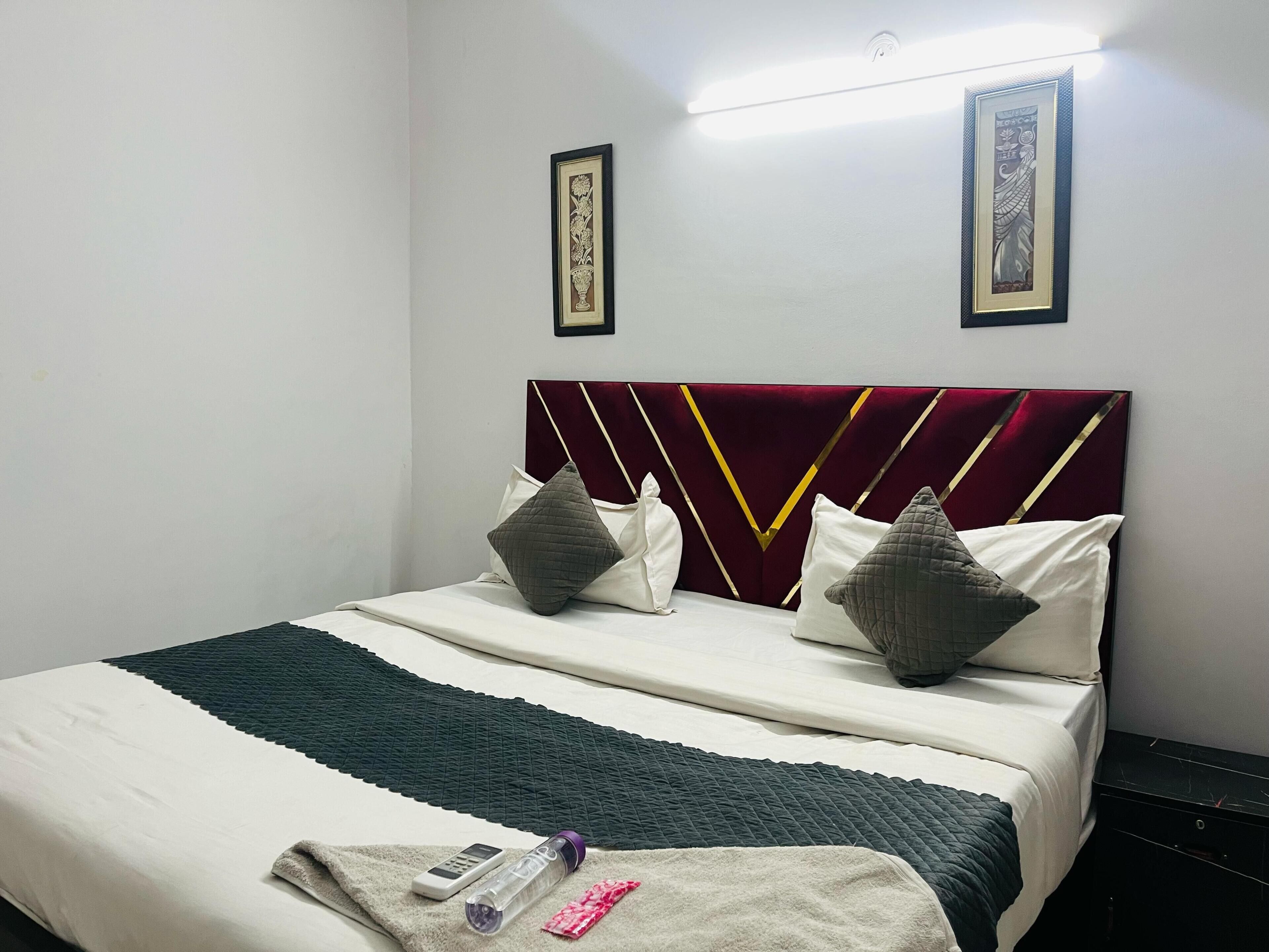 A hotel room with a bed, a blanket, a pillow, a remote control, and a water bottle.