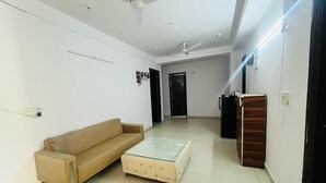 A living room with a sofa, ottoman, ceiling fan, and a door leading to another room. - Roomshala 045 Galaxy Noida 35 (Noida)