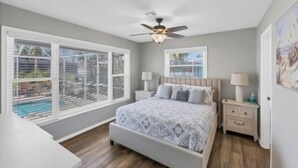 Un dormitorio con cama, mesitas de noche, ventilador de techo y una ventana con persianas.