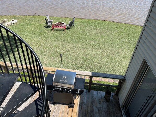 Una terraza con una parrilla, con vistas a un área verde con sillas y una mesa.