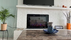 A living room with a fireplace, a flat-screen TV mounted above it, and a sign indicating 'TO LAKE'. - 3-bedroom home,  waterfront patio,  fishing, kayaking, swimming, yoga room  (Trinity)