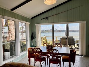 Un comedor con una mesa y sillas, ventanas amplias con vista a un lago y un ventilador de techo.