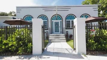 Un bâtiment à la façade blanche, doté d’une entrée fermée par un portail et d’un chemin menant à la porte.