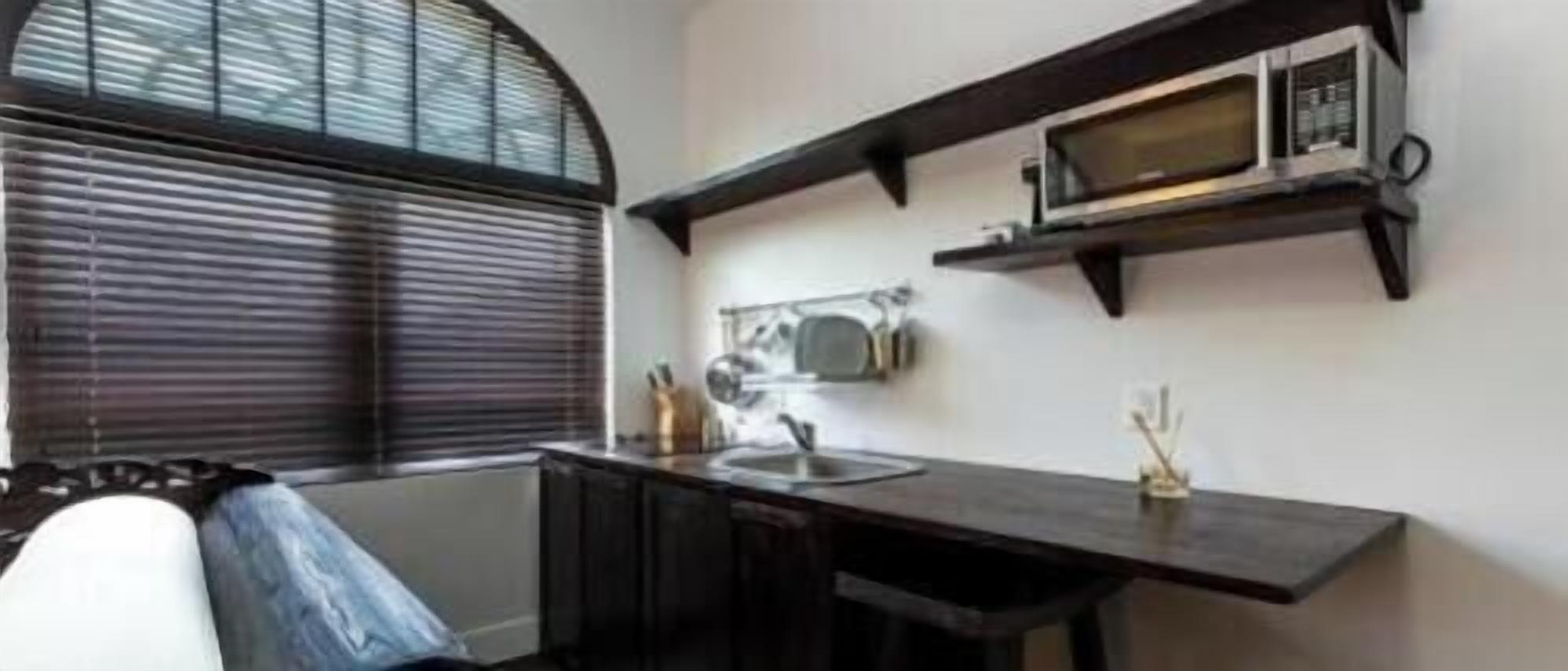 A kitchen with a microwave, a sink, and a window with blinds.