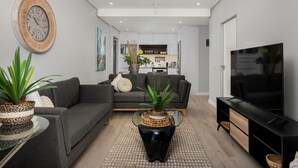 A modern living room with a grey sofa, a black coffee table, a TV, and a kitchen in the background. - Stylish and Modern Apartment with City Views (Cape Town)