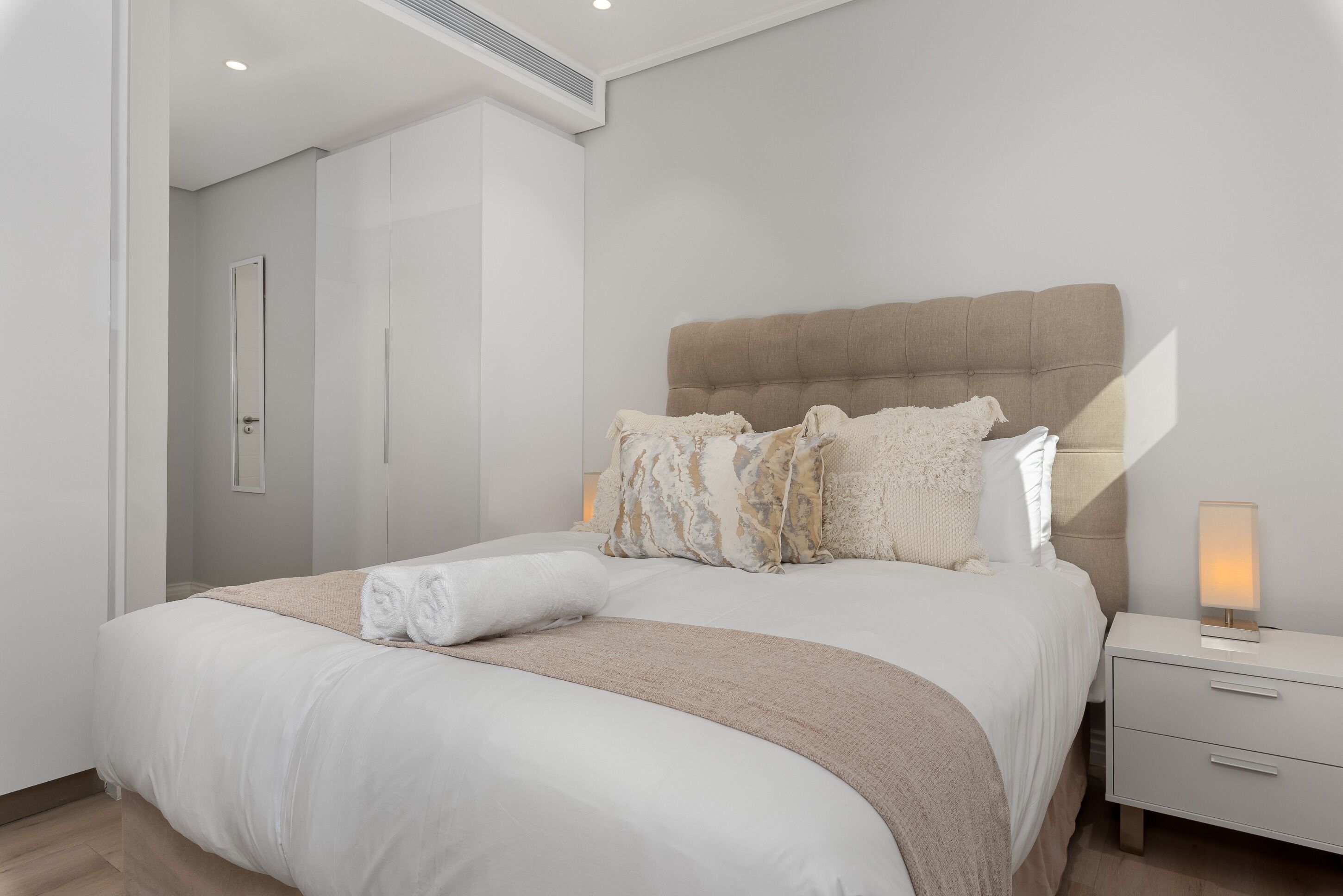A modern bedroom with a large bed, a bedside table, and a wall-mounted light.