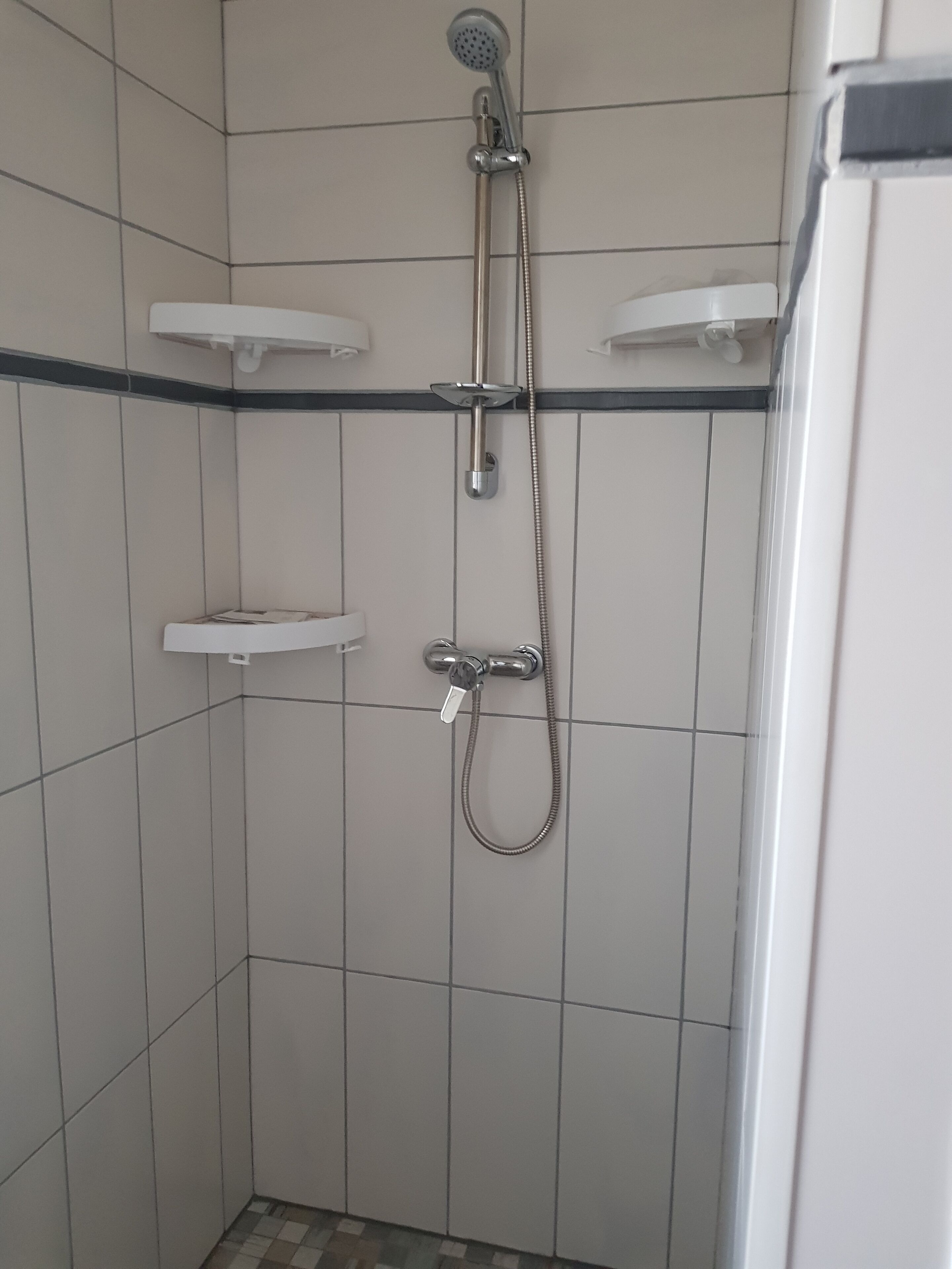Eine kleine, mit Fliesen ausgekleidete Duschkabine mit Handbrause und Duschvorrichtung.
