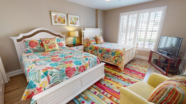 A bedroom with two beds, a TV, and a window with blinds. - Desoto Beach Club 105 | Ocean Views, Resort Pool (Tybee Island)