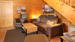 A cozy log cabin interior with a wooden staircase, a leather sofa, a wooden coffee table, and a lamp.