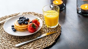 Ontbijt met pannenkoeken, bessen en sinaasappelsap op een geweven placemat.