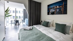 Een moderne hotelkamer met een groot bed, een schilderij van een stadsgezicht en uitzicht op de stad door het raam.