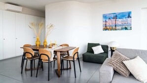 A modern living room with a dining area, a green sofa, and a painting of a cityscape. - Corner Apartment (Bruxelles)