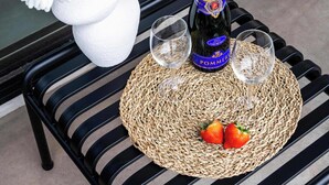 A table with a bottle of champagne, two glasses, a woven placemat, and a vase with flowers. - Corner Apartment (Bruxelles)