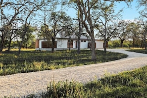 Una casa con camino de grava, rodeada de árboles y césped.