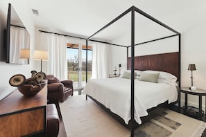 Una cama con dosel, un cabecero de madera, un sofá, una mesita de noche con una lámpara y un espejo grande.