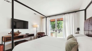 Ein Schlafzimmer mit Bett, Schreibtisch, Stuhl, Fernseher und einem Fenster mit Vorhängen.