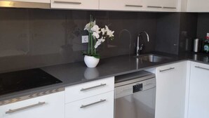 A modern kitchen with white cabinets, a black countertop, a stainless steel dishwasher, and a vase with white flowers. - semi-detached house with pool 3 bedrooms near the beach (Platja d'Aro)