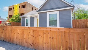 A single-story house with a grey siding exterior, a front porch, and a wooden fence. - Charming 4BR/2BA Only 5 mins Downtown & Riverwalk (San Antonio)