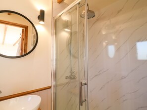 A modern bathroom with a glass-enclosed shower, a round mirror, and a white sink. - Buzzards (Crediton)