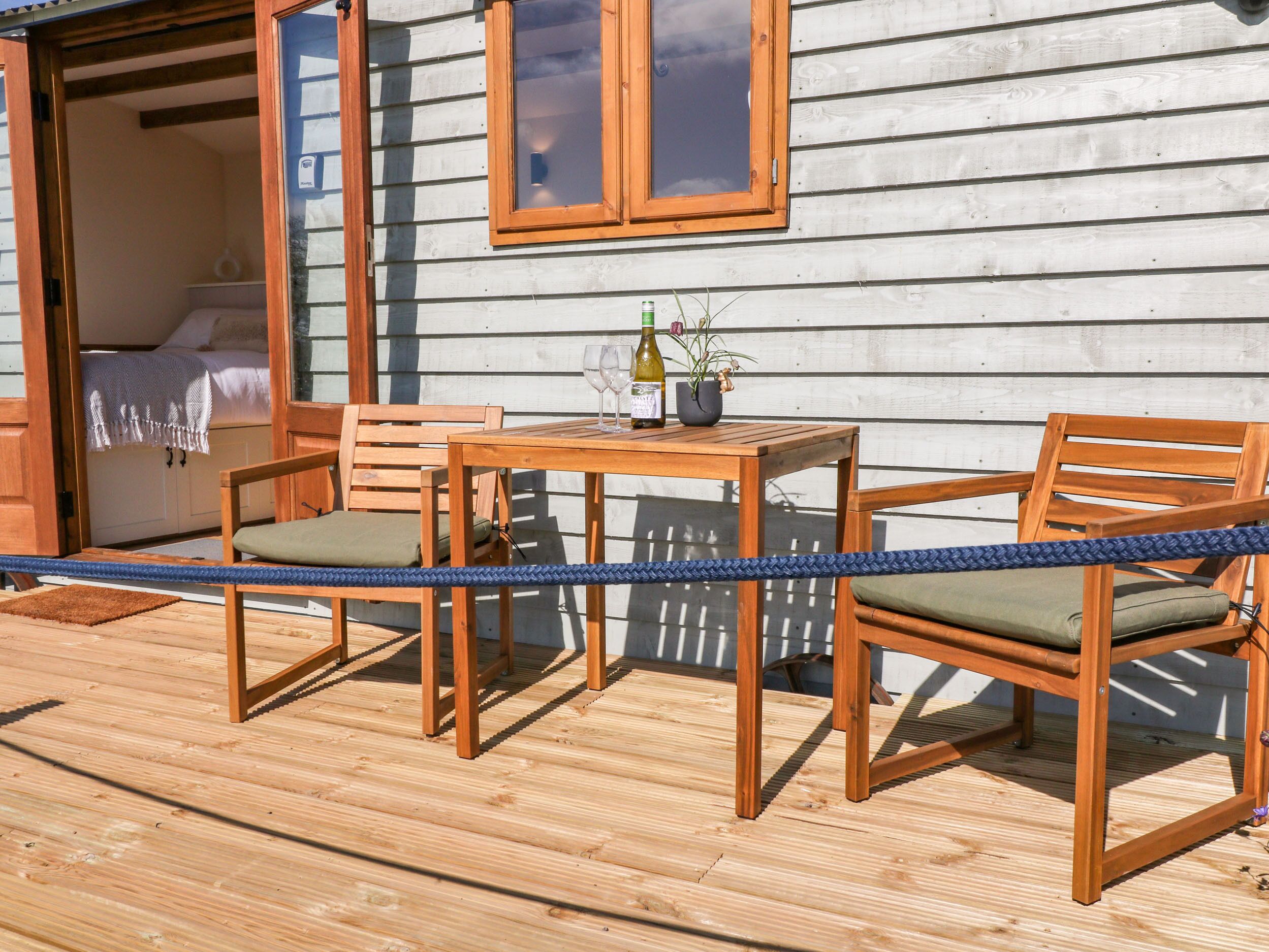 A wooden deck with a table and chairs, a bottle of wine, and a potted plant.
