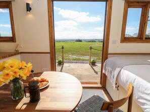 A cozy room with a wooden table, a bed, and a view of a green field through an open door.