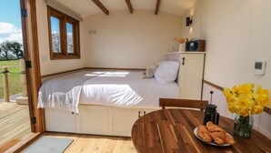 Une chambre confortable avec un lit, une petite table sur laquelle est posé un vase de fleurs et un plafond en bois.